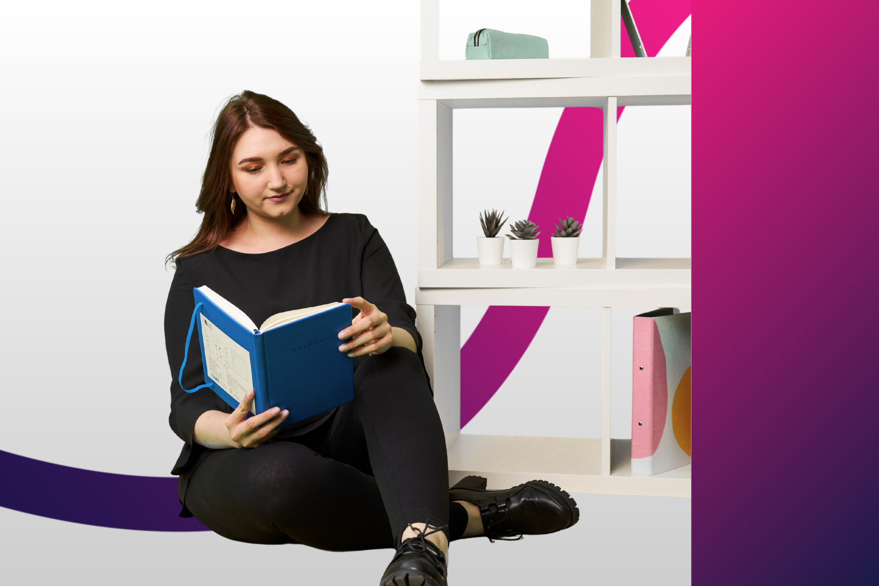 Młoda dziewczyna siedzi na podłodze i czyta książkę, obok niej stoi lekki, biały regał