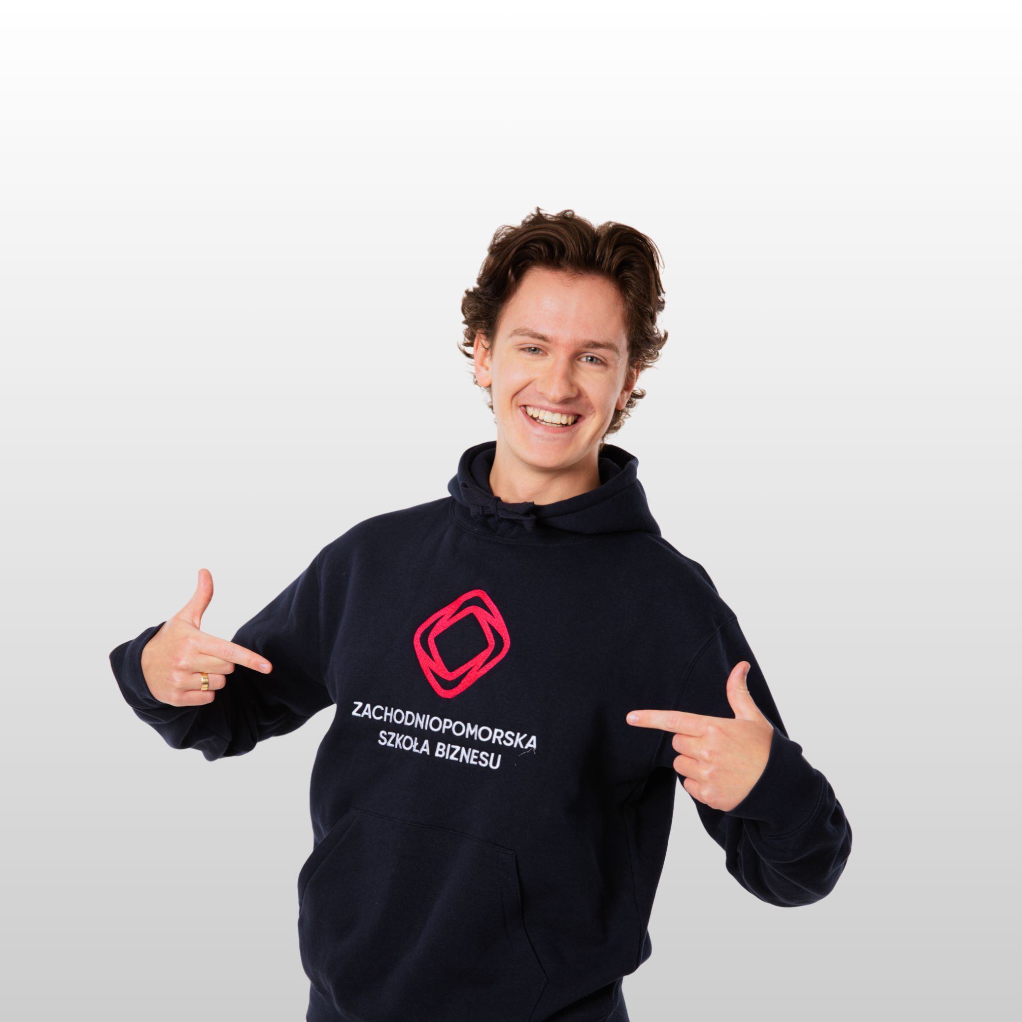 Młody uśmiechnięty mężczyzna, ubrany w granatową bluzę z logo ZPSB, wskazuje na nie palcami