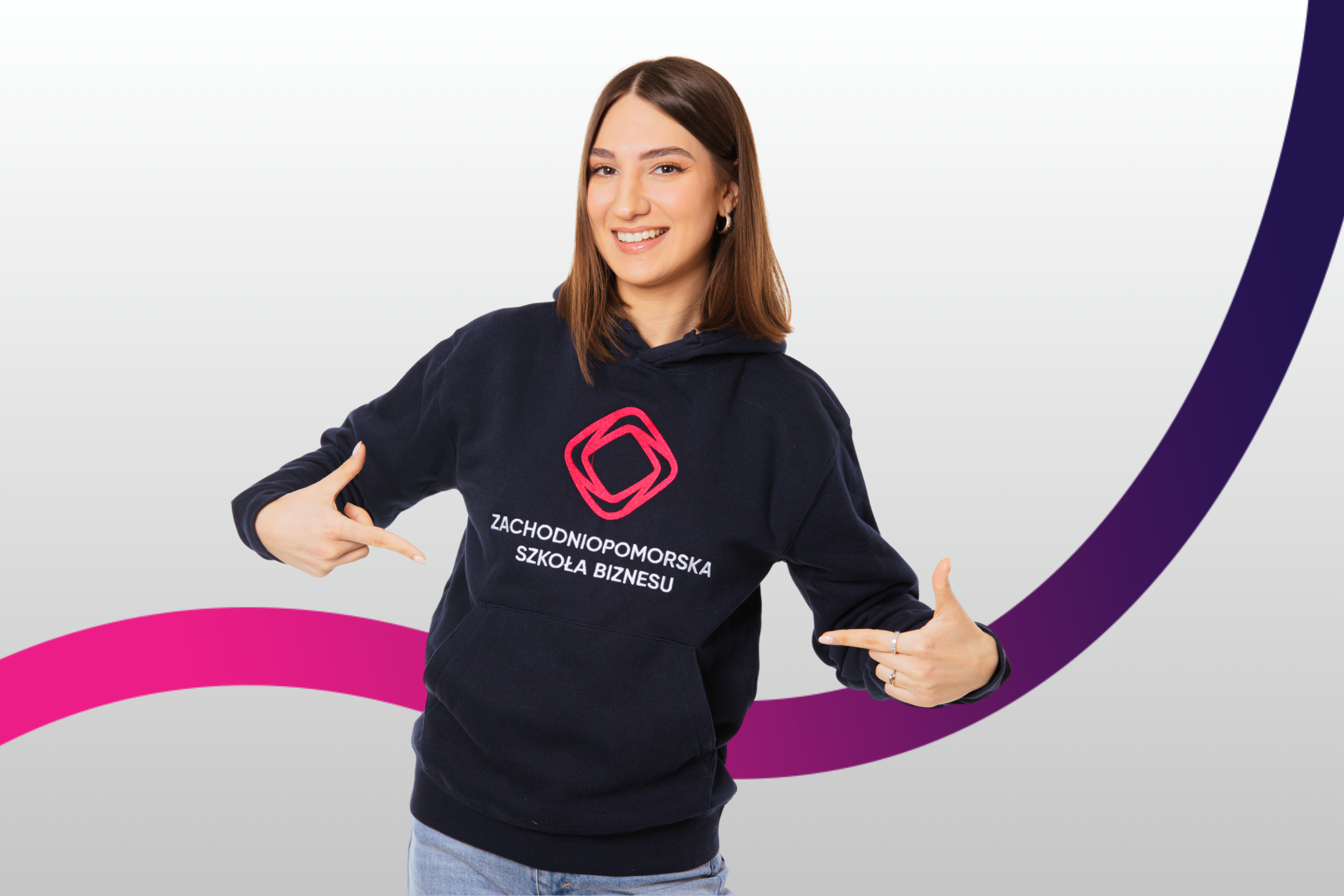 Uśmiechnięta dziewczyna ubrana w granatową bluzę z logo ZPSB pokazuje na nie palcami