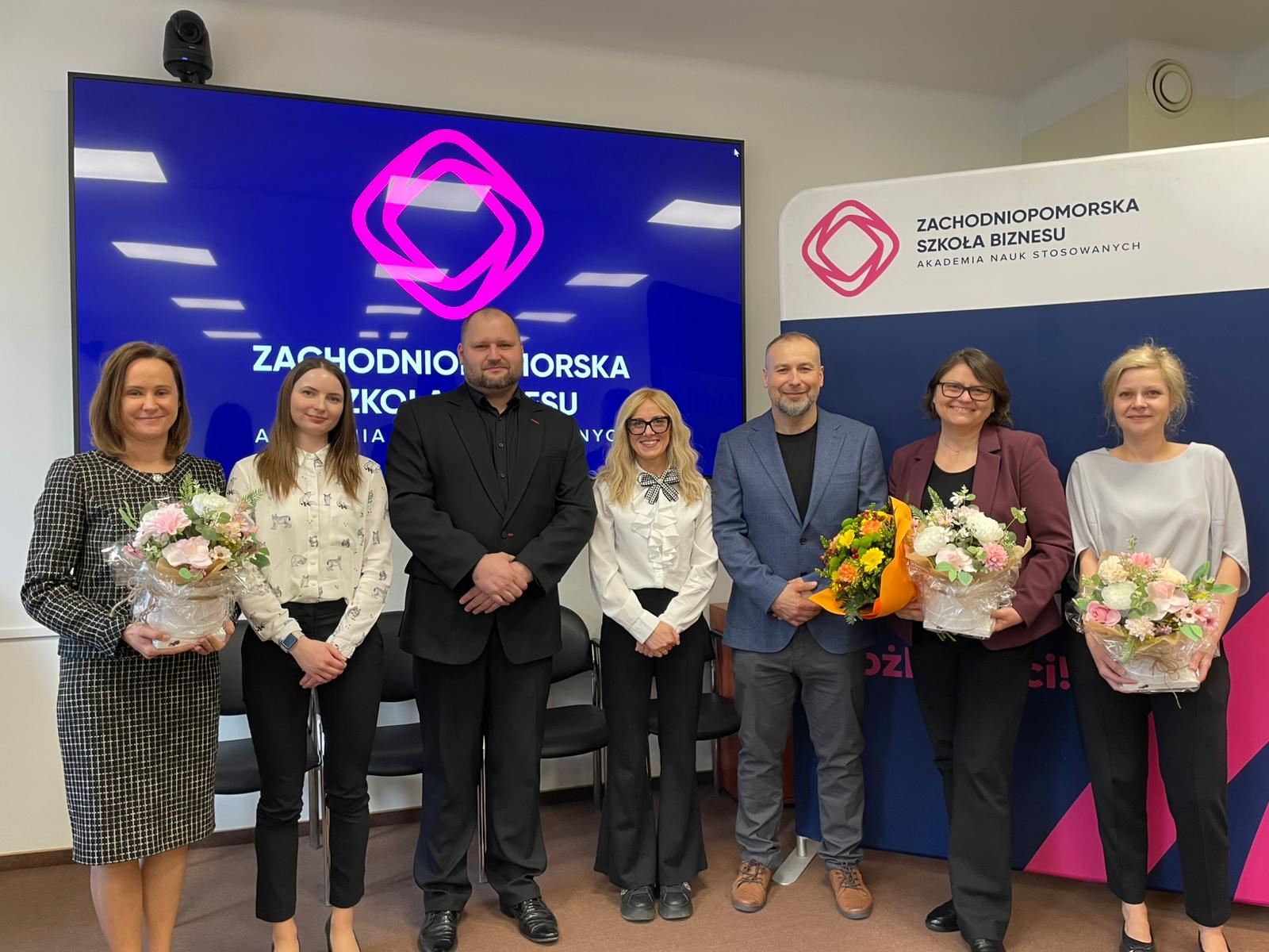 Absolwenci z komisją pozują na tle telewizora z wyświetlanym logo ZPSB