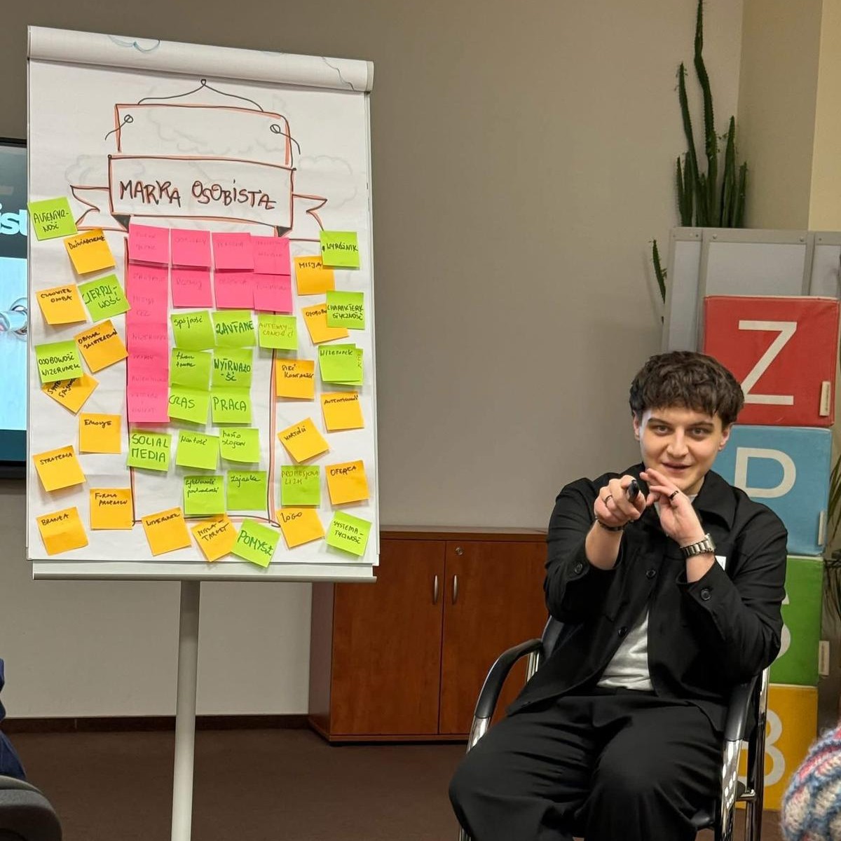 Prowadzący warsztat prezentuje elementy marki osobistej przy tablicy z notatkami.
